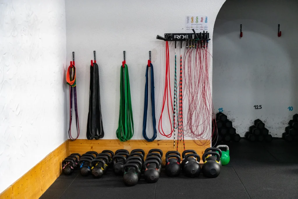 Widerstandsbänder und Springseile an der Wand, darunter eine Reihe Kettlebells auf dem Hallenboden