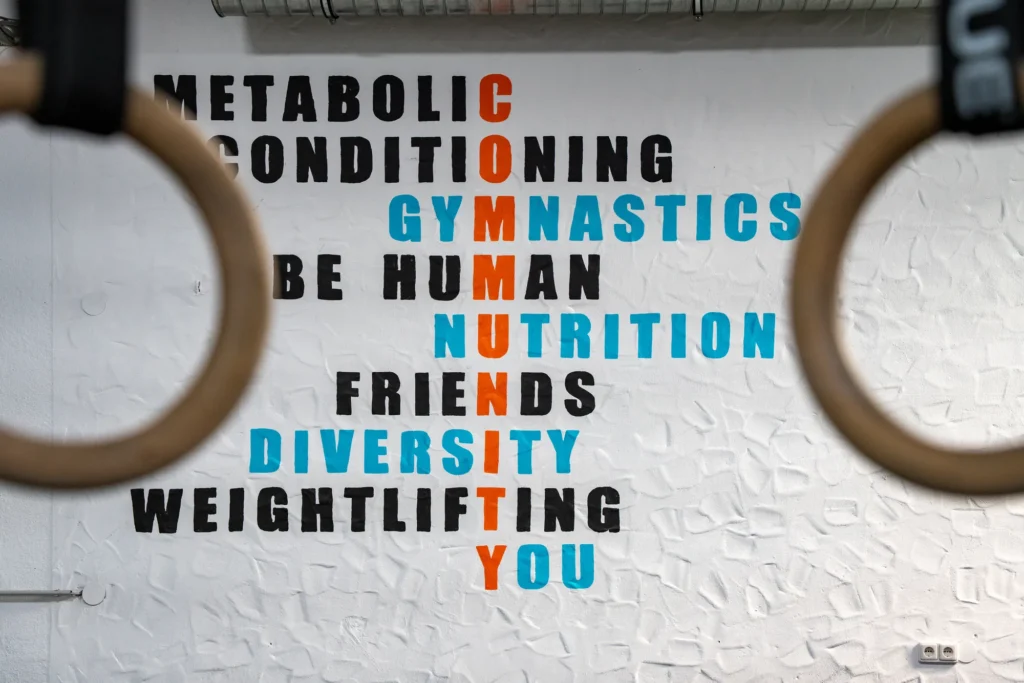 Blick durch zwei Turnringe auf die Motto-Wand mit den Begriffen Community, Gymnastics, Nutrition, Friends und You