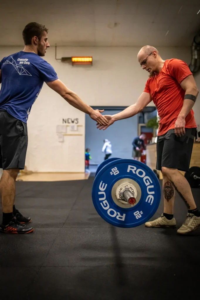 Zwei Athleten klatschen sich beim Team-WOD bei CrossFit am See ab, zwischen ihnen eine Hantelscheibe